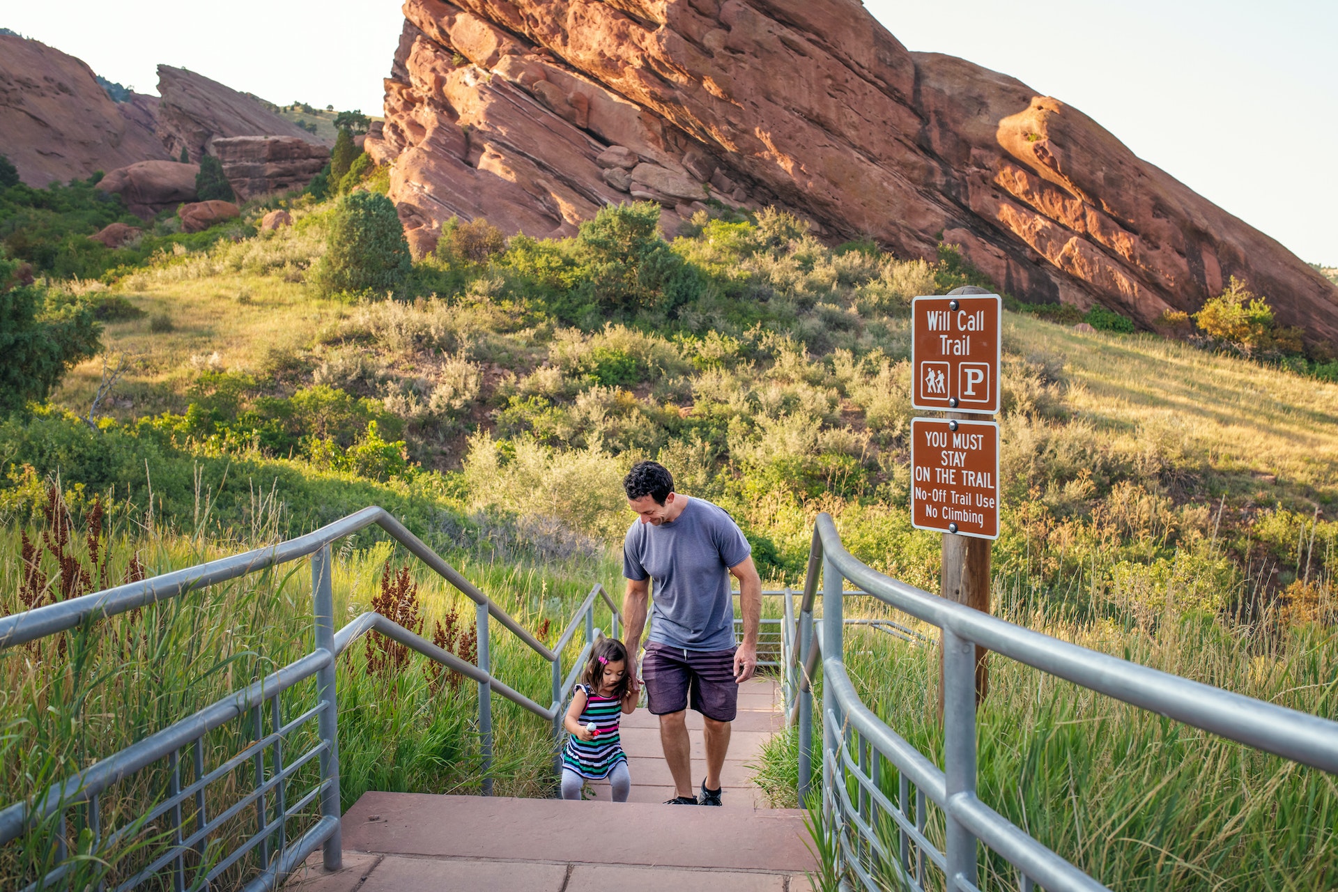 A father has fun helping his toddler daughter who is jumping up the stairs at Red Rock Park, Colorado