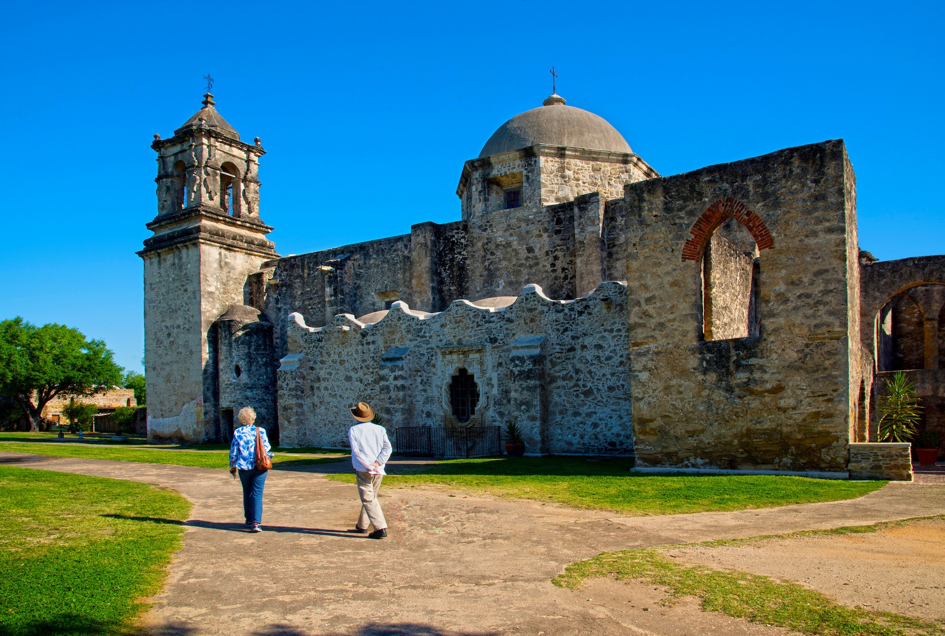 Two people walk on the grass in front of a historic religious building