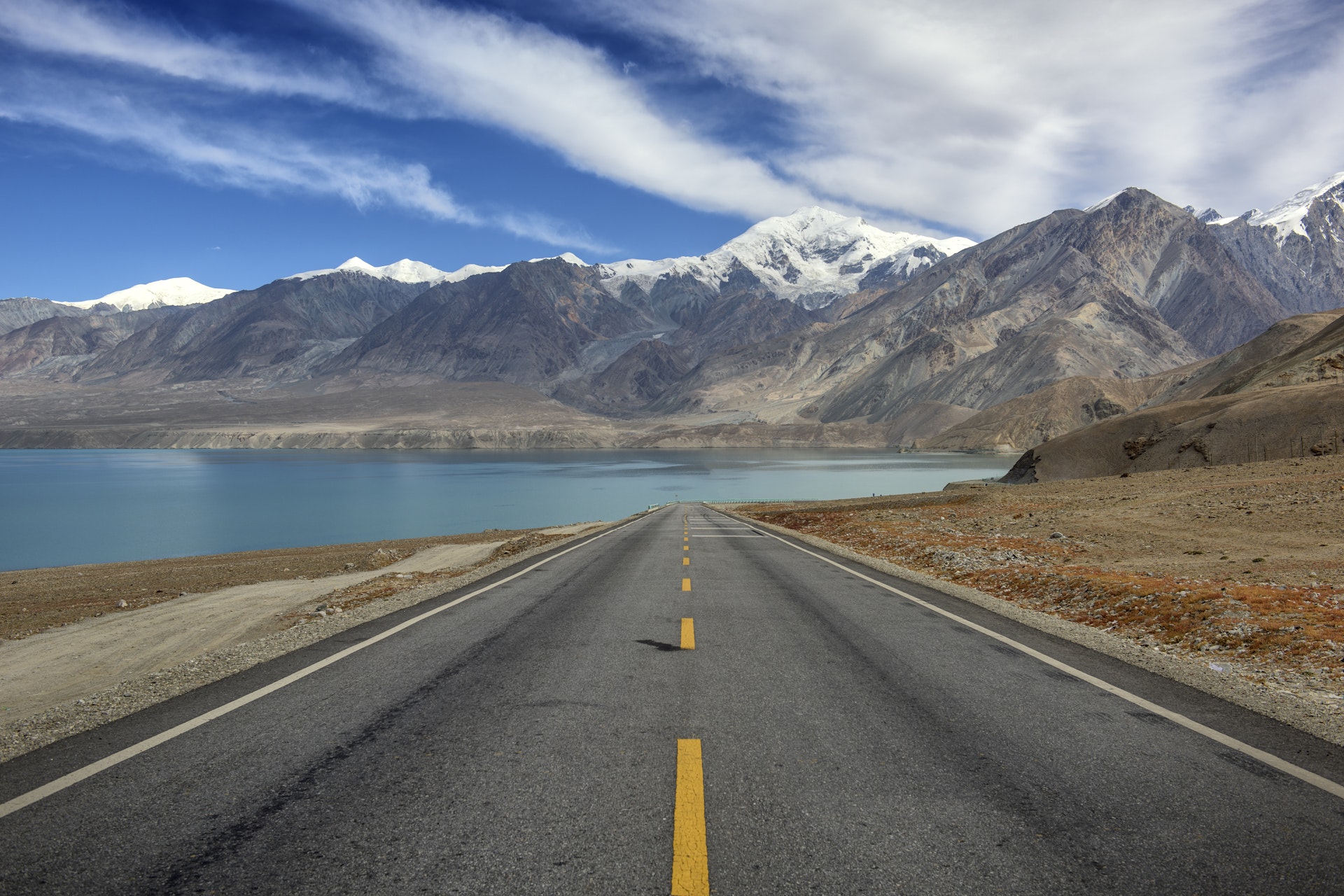 A long empty stretch of the Karakoram Highway with mountain peaks in the background