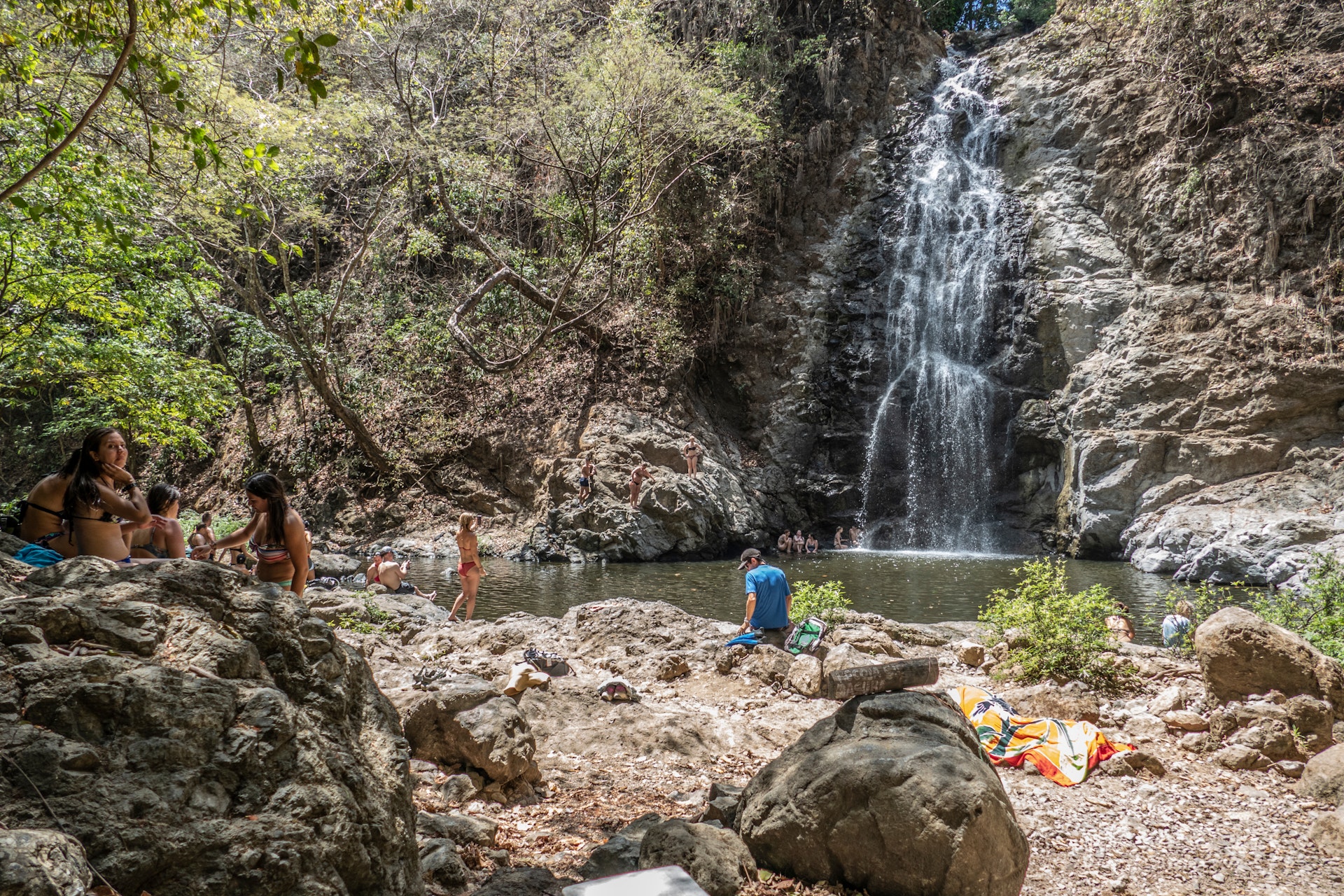 Small groups of people in bathing suits gathered on the rocky ground around Montezuma Falls in Costa Rica