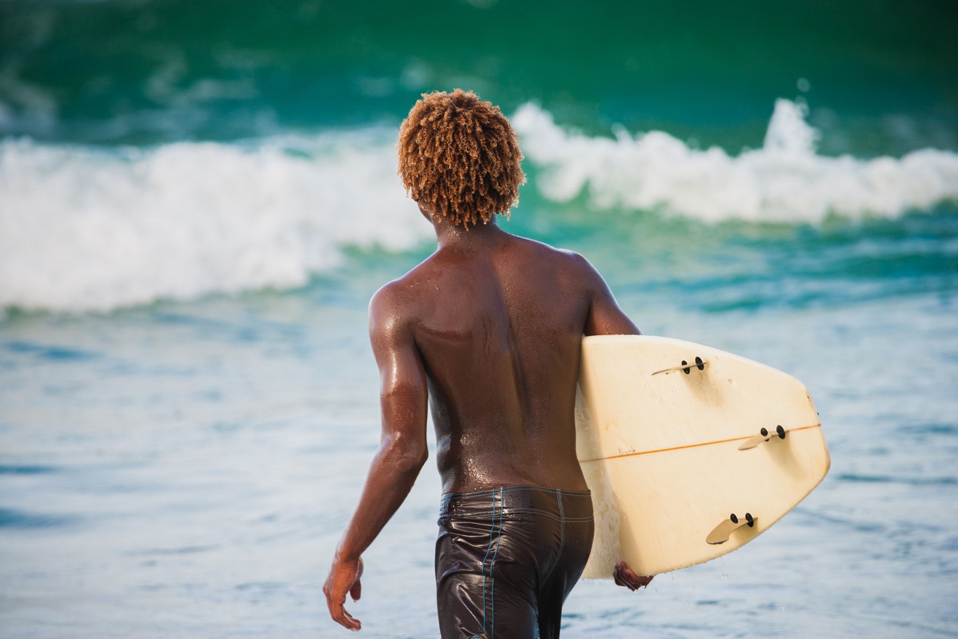 Young adult male surfer studying the waves before entering, seen from behind.